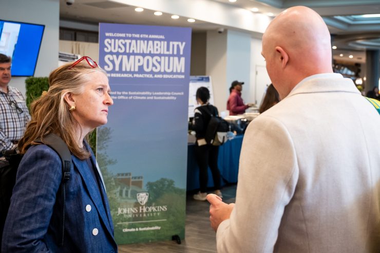 Two event attendees talk in front of large sign reading "Sustainability Symposium."