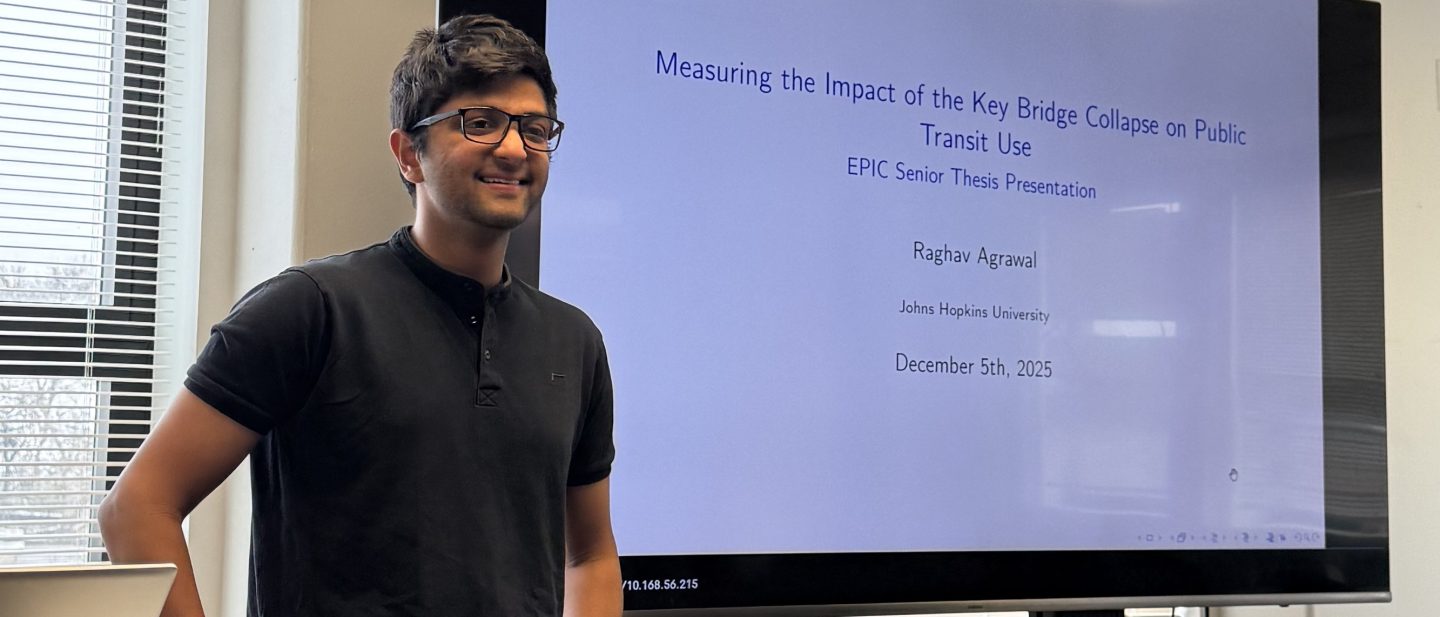 Raghav Agrawal stands in front of a projector screen as he presents on his research.