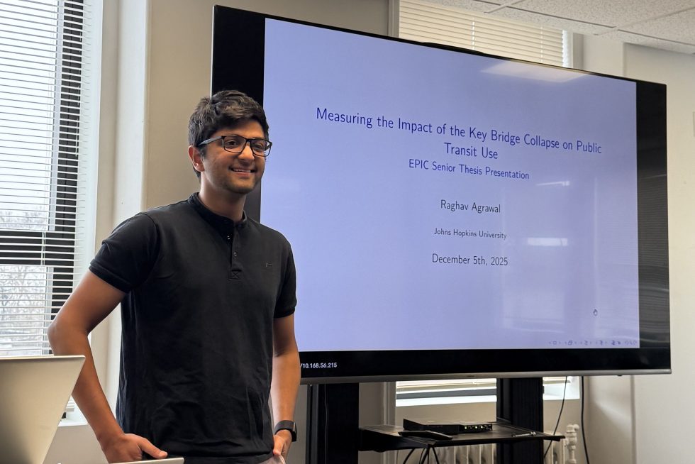 Raghav Agrawal stands in front of a projector screen as he presents on his research.