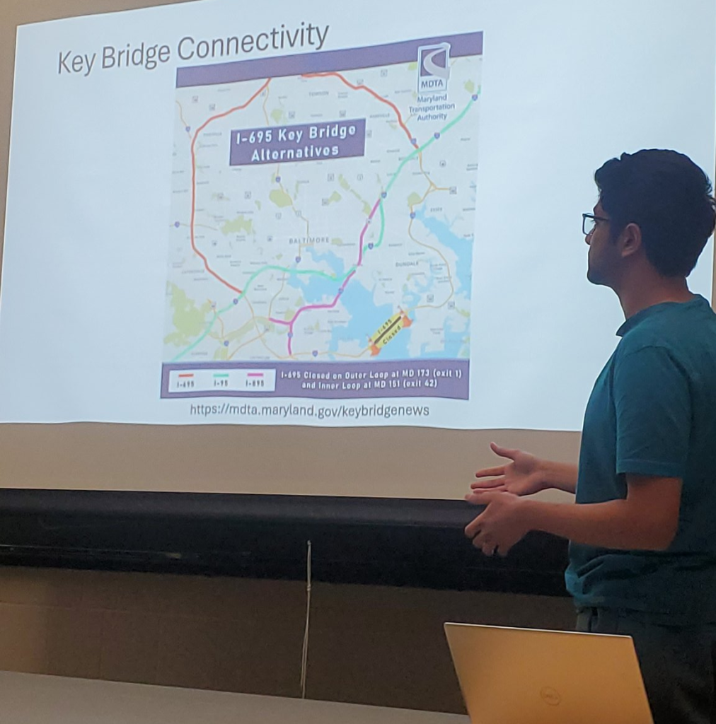 Raghav Agrawal stands in front of a projector screen as he presents on his research.