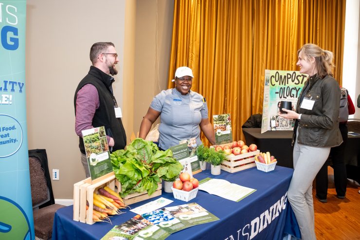 Event attendees talk at an informational table featuring Hopkins Dining and a display of local produce.