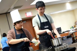 2 Hopkins students cooking together, both wearing "Hopkins Dining" aprons. 